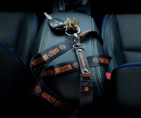 A set of keys on a branded Harley-Davidson lanyard rests on a car seat, secured by the seatbelt, symbolizing safety and brand loyalty.