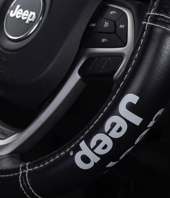 Steering wheel with the "Jeep" logo in focus, buttons visible, and the wheel partially wrapped in a leather cover, inside a vehicle cabin.