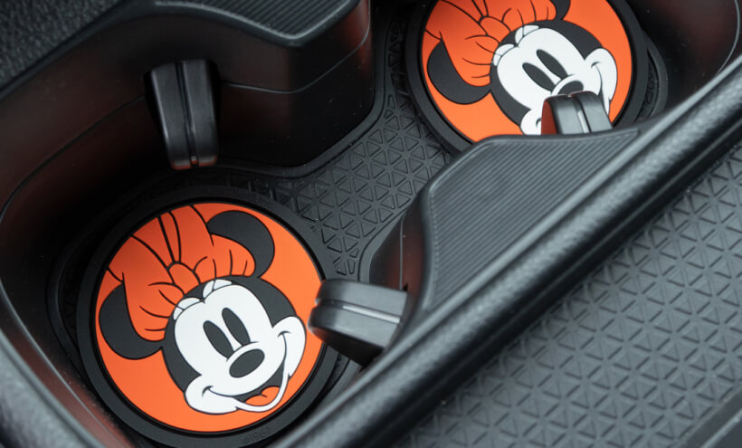 Car cup holders contain coasters with a cartoon character's face; a black, textured pattern surrounds them.