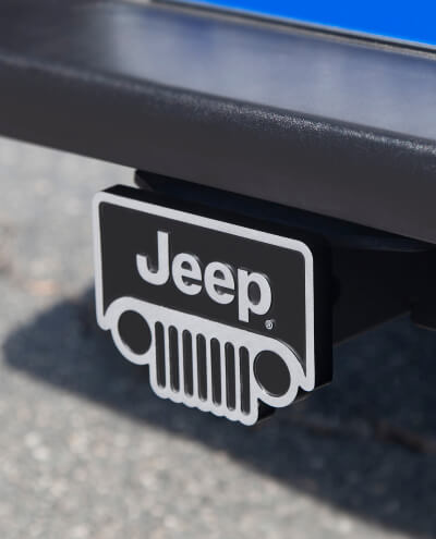 A black and white Jeep logo hitch cover attached to a vehicle, with a blurred background indicating an outdoor setting.