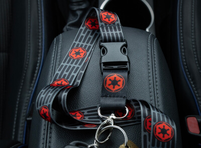 A black backpack with red and black patterned straps rests against a car seat, with a metal ring and keys attached.