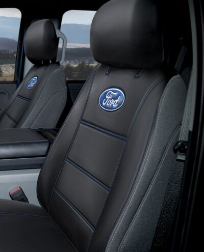 Black car seats with the Ford logo, positioned inside a vehicle, with a window view of a blurred natural landscape.