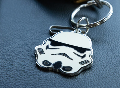 A keychain featuring a stormtrooper helmet rests on a textured surface, likely the interior of a vehicle.