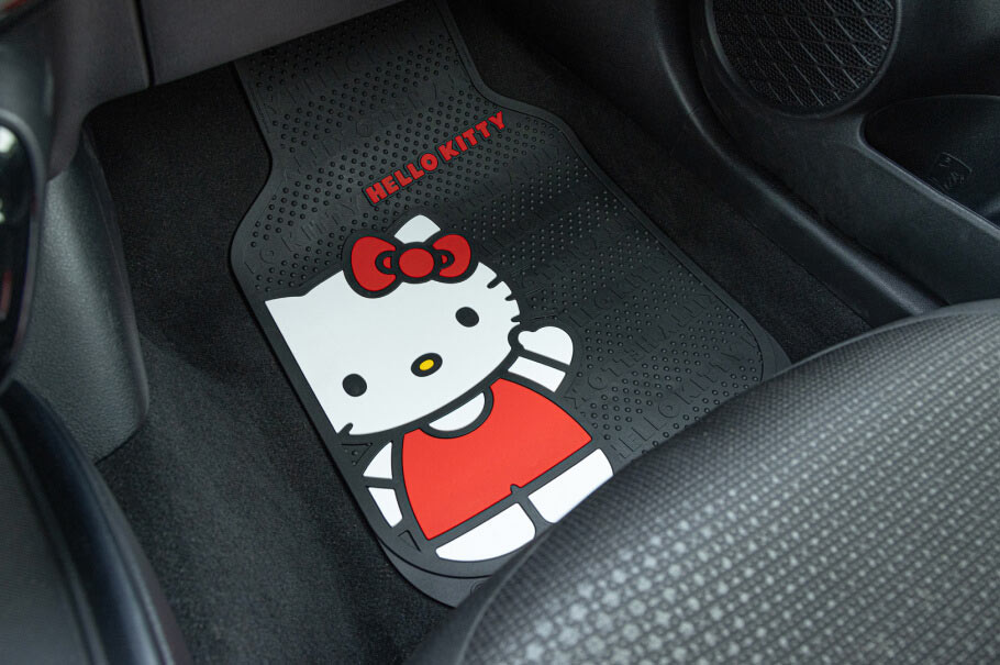 A Hello Kitty car floor mat is placed in a vehicle, bearing the character's likeness and the text "Hello Kitty." The context is a car's interior.