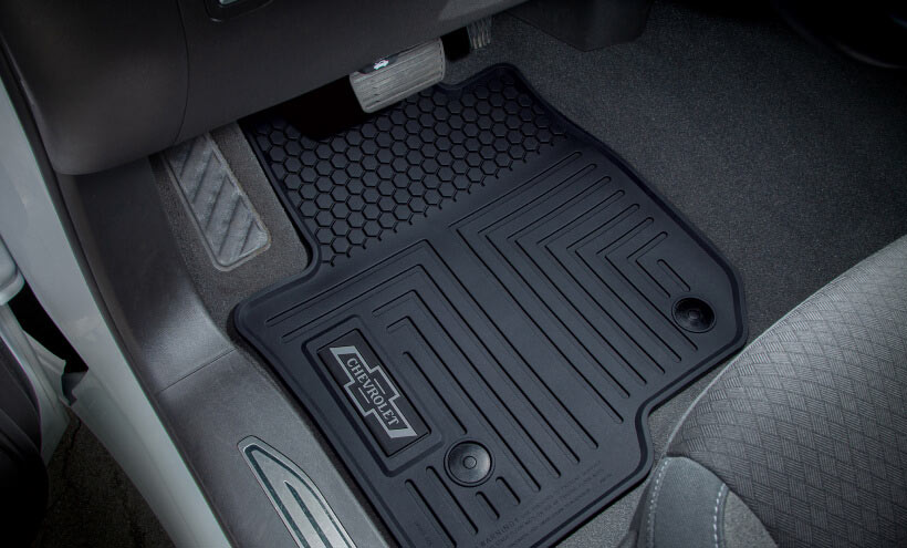 A black, textured car floor mat rests on the driver's side of a vehicle interior, featuring a design and brand logo: "WeatherTech".